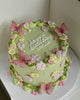 Pastel green buttercream round cake with pink wafer butterflies, floral piping, pearls, and 'happy birthday cassie' text