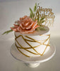 White fondant round cake with gold geometric lines, peach sugar roses, green leaves, and a gold Happy Birthday Mom topper