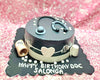 Black and grey round birthday cake with stethoscope topper, white ECG line, heart plaque, RX scroll and pill bottle accents