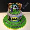 Round fondant cake with LEGO-style Batman and Joker toppers, gray sides, green top, Batman logo and city skyline