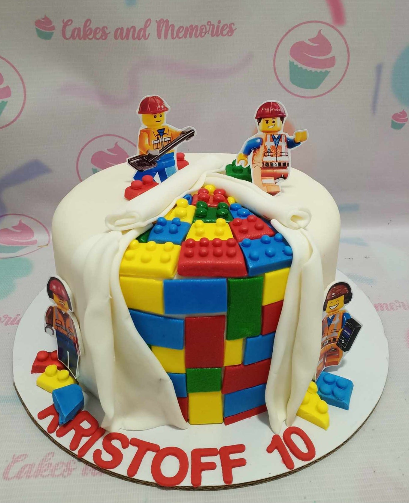 A vibrant Lego cake featuring smooth white fondant, adorned with colorful edible Legos and themed construction printout toppers. This fun, one-tier design is perfect for children's birthday celebrations.