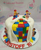 A vibrant Lego cake featuring smooth white fondant, adorned with colorful edible Legos and themed construction printout toppers. This fun, one-tier design is perfect for children's birthday celebrations.