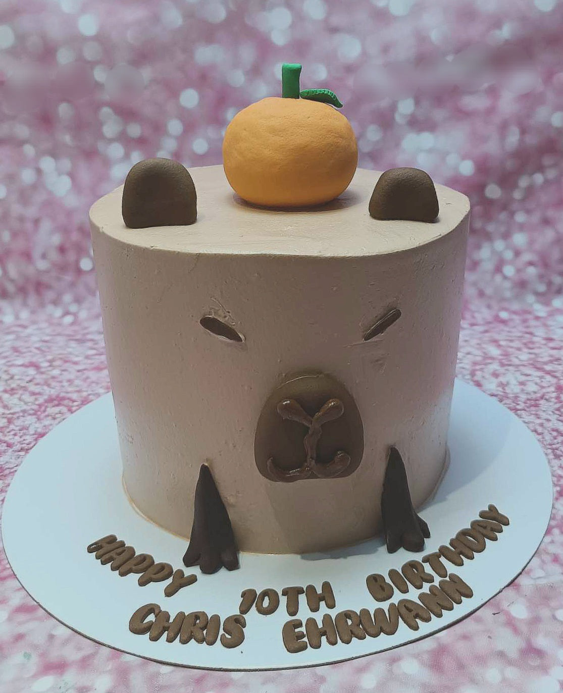 This adorable Capybara Cake features a charming brown capybara design, perfect for celebrating Chris Ehrwann's 10th birthday. Accented with orange details, it's a delightful centerpiece for any birthday party.