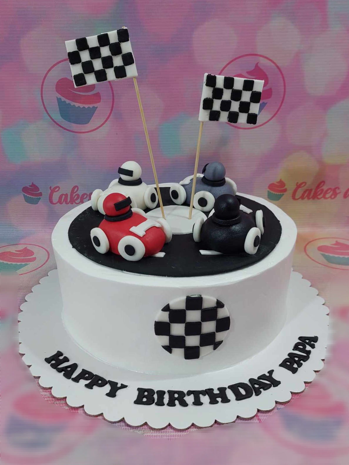 This custom Wheels Cake features a sleek 1-layer design highlighting exciting racing elements like checkered flags and colorful printout toppers of race cars, perfect for kids' cart races. Ideal for a birthday celebration, it's a fantastic choice for dads and little racers alike.