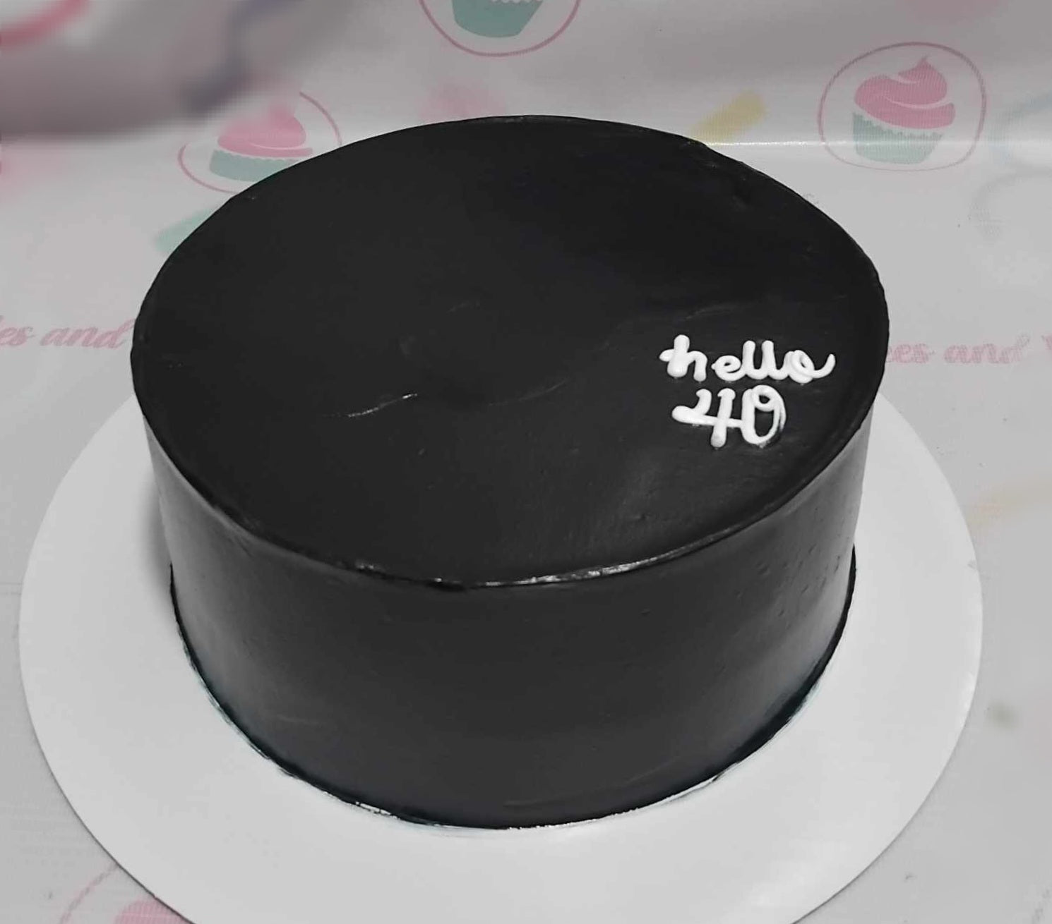 A sleek minimalist cake in black adorned with a simple "Hello 40" printout topper, perfect for celebrating a 40th birthday for any man or woman. This one-tier design captures elegance and sophistication for a memorable occasion.