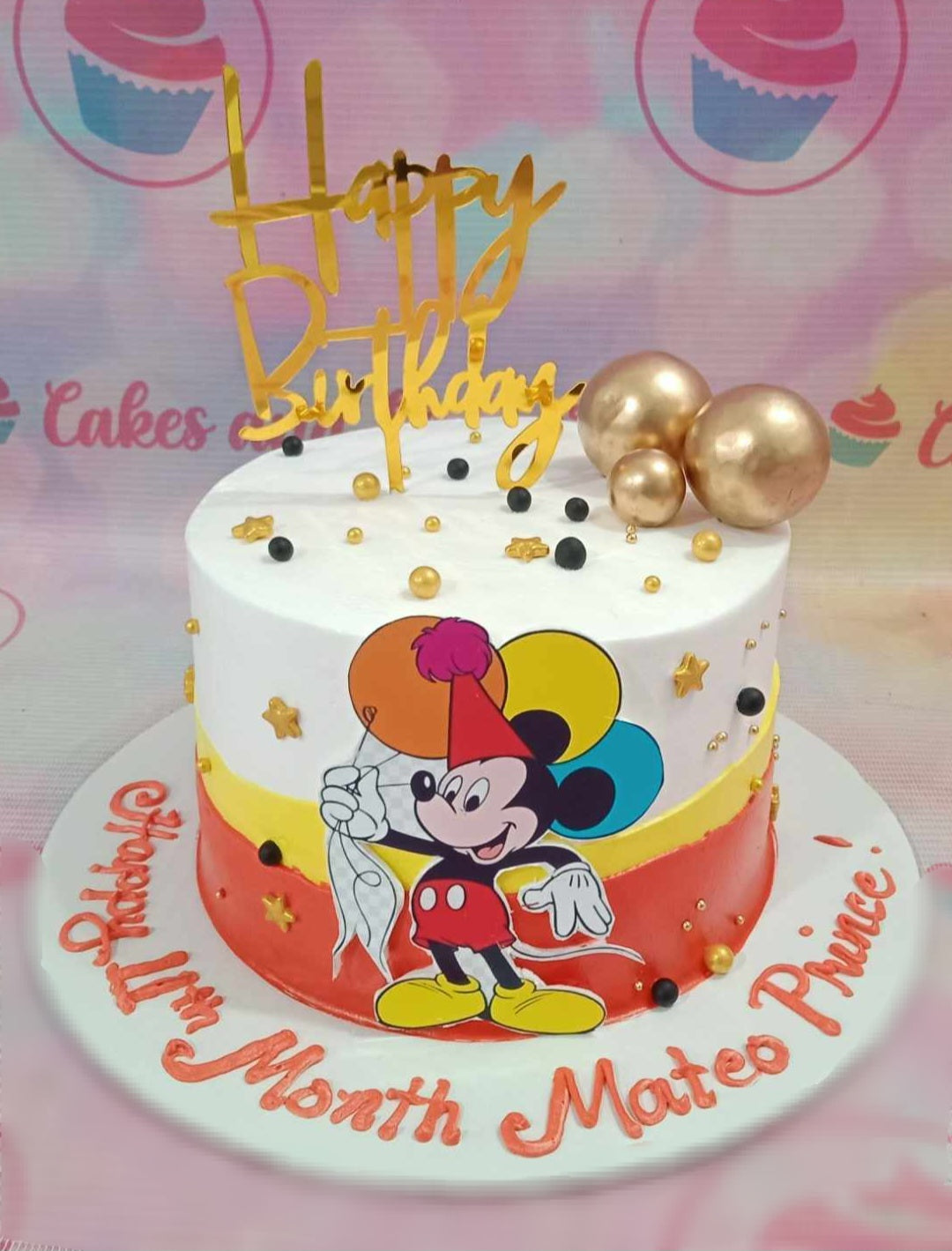 A delightful Mickey Mouse Cake features a charming white and red design adorned with colorful balloons and golden balls, perfect for a baby toddler's 1st birthday celebration. It showcases playful printout toppers and is a one-tier, one-layer masterpiece that any child will love.