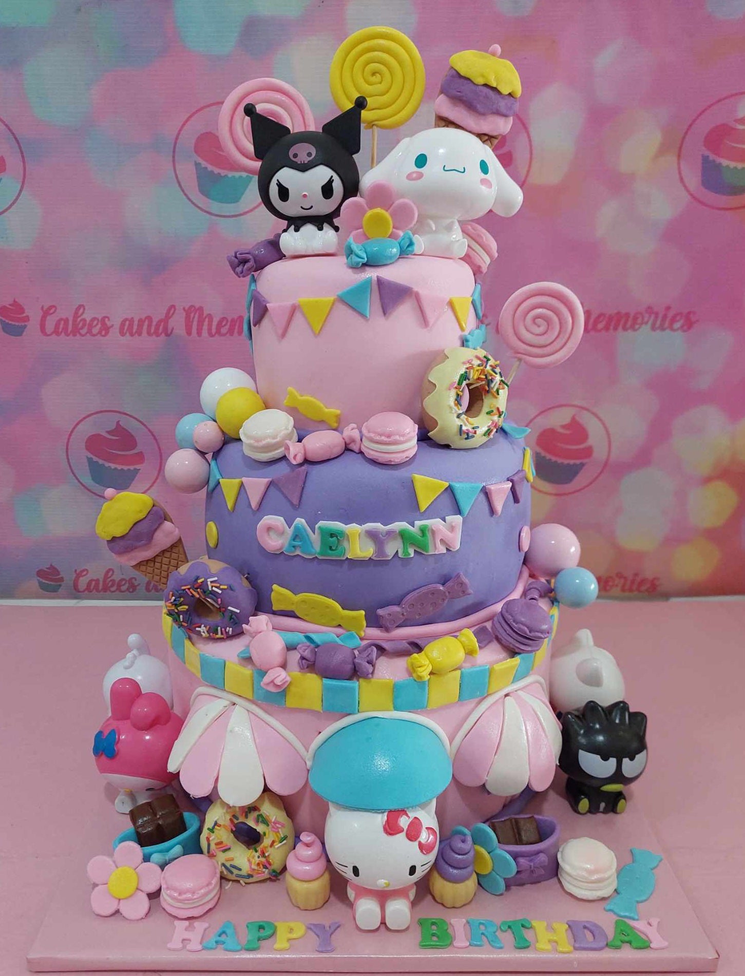 This multi-tiered Hello Kitty cake features colorful fondant designs with adorable character accents like Kuromi, Cinnamoroll, and My Melody. Adorned with sprinkles, macarons, donuts, lollipops, and cute flags, it’s perfect for any birthday celebration.