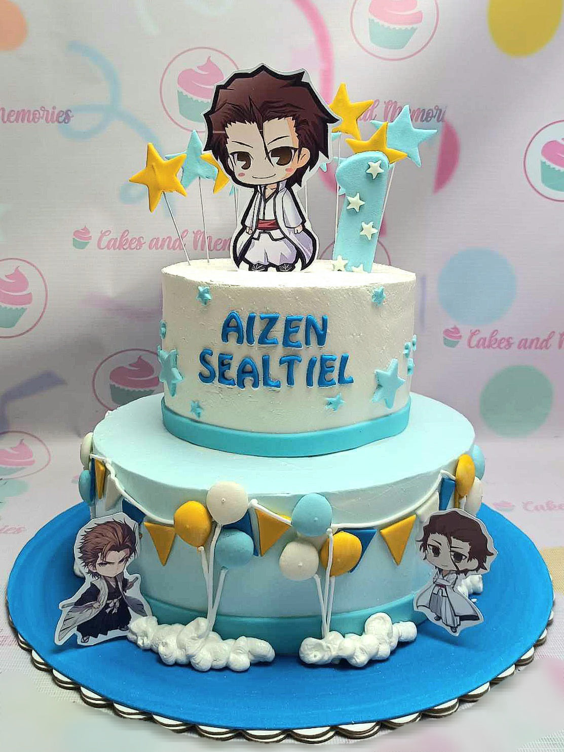 This stunning 2-tier anime cake features a white base adorned with blue accents, playful balloons, and shining stars, perfect for a 1st birthday celebration. Decorated with printout toppers of Sosuke Aizen from Bleach, it beautifully captures the essence of Japanese anime artistry.