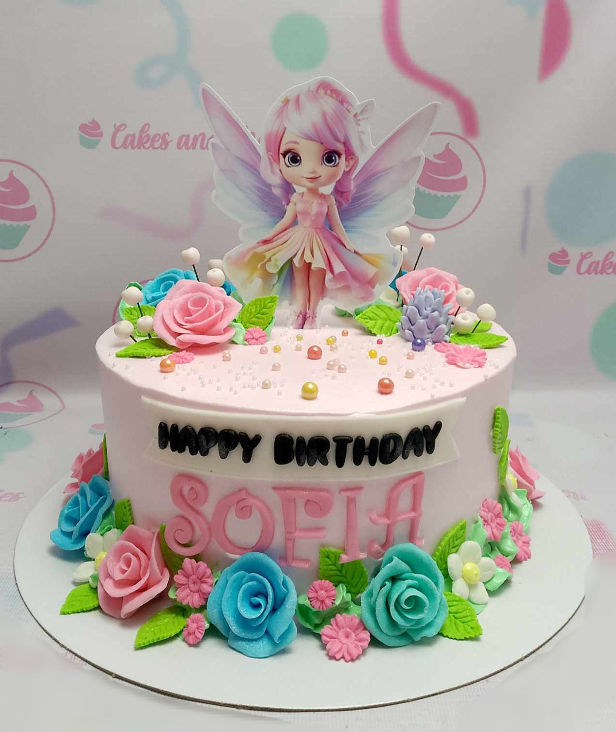 A charming pink fairy cake adorned with delicate flowers, roses, and leaves, featuring elegant pearls and themed printout toppers for the birthday girl Sofia. This one-tier design perfectly captures the magic of a fairy-themed celebration.