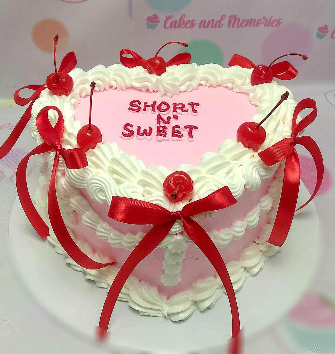 This vintage cake features a charming heart-shaped design in pink, adorned with cherries and red ribbons. It embodies a cute aesthetic with its single tier, ideal for any special occasion.