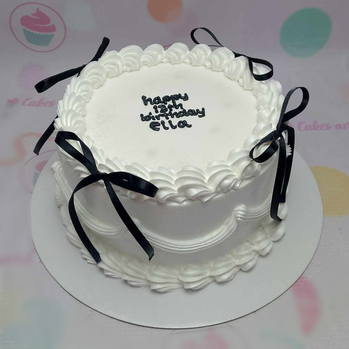 A stunning vintage cake designed for Ella's 13th birthday, featuring elegant white swirls and delicate black bows. This one-tier masterpiece is adorned with a chic black ribbon, perfect for celebrating a special milestone.