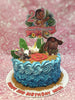This Moana-themed cake features blue ombre icing rosettes and is adorned with printout toppers of Baby Moana, Maui, Pua, and Hei Hei, alongside tropical leaves and flowers, capturing a sand beach vibe for Mika's 2nd birthday. The cake is a single tier with eye-catching details perfect for a memorable celebration.
