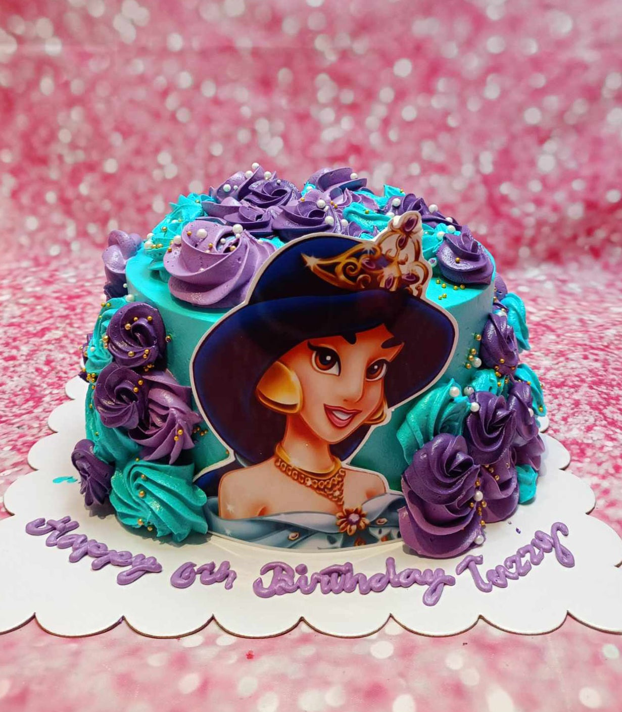 This custom Jasmine Cake features a stunning teal and purple rosette design, adorned with gold sprinkles and printout toppers inspired by Aladdin for a magical 6th birthday celebration. The single layer and tier showcase enchanting details, perfect for any Disney fan.