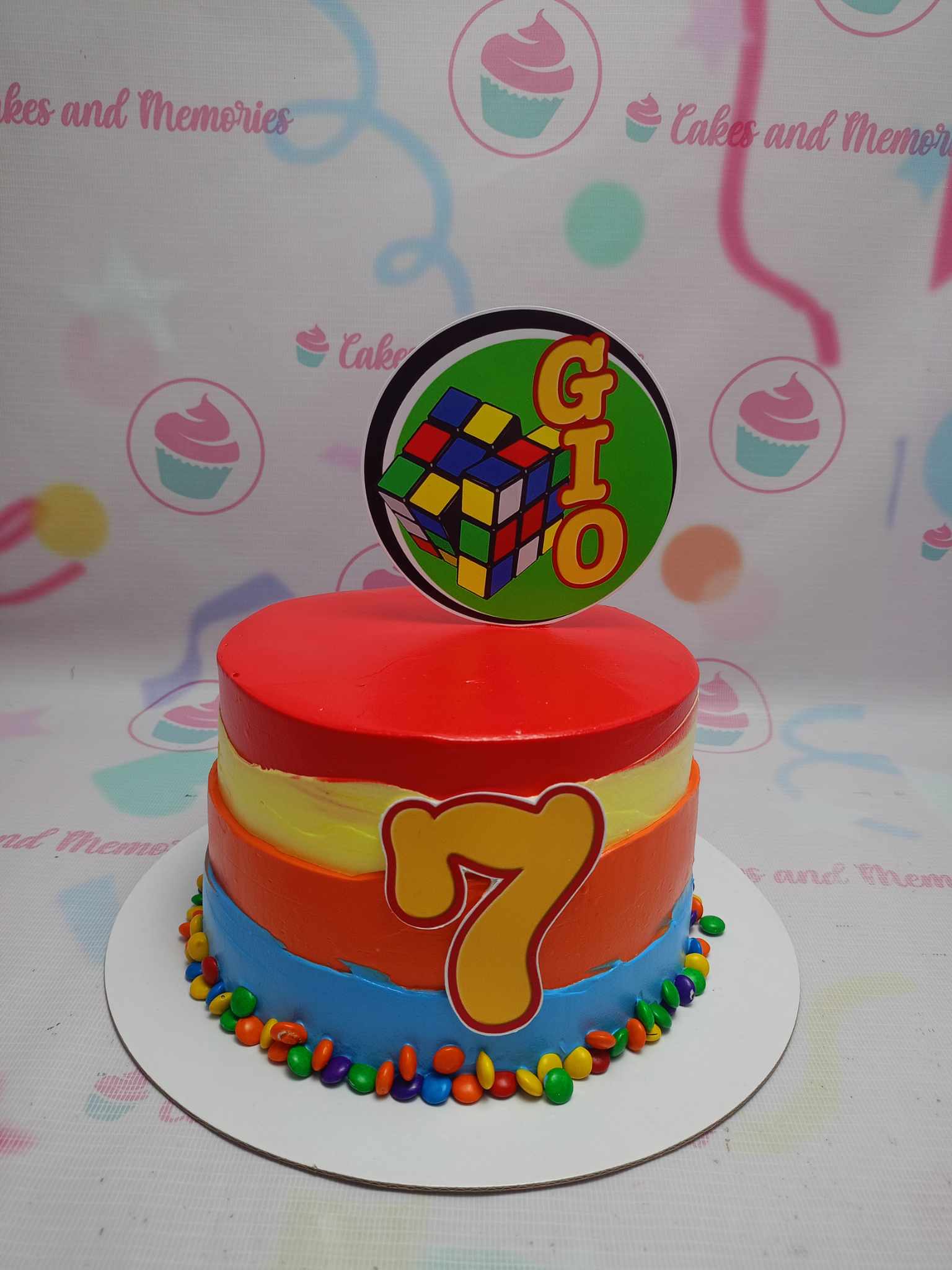 Celebrate a 7th birthday with our vibrant Rubik's Cube Cake, featuring bold red and orange colors that capture the essence of this beloved toy and math puzzle. Adorned with playful printout toppers, this colorful one-tier cake is the perfect centerpiece for a fun birthday bash!