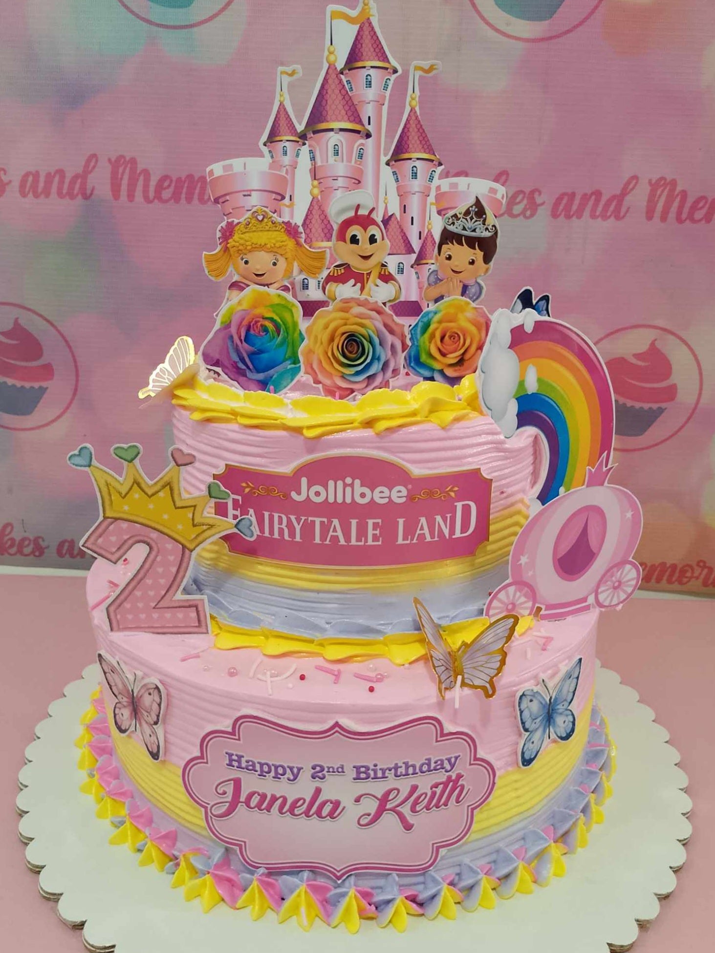 A stunning two-tiered Jolibee cake features a charming pink castle surrounded by colorful butterflies and flowers, perfect for a fairytale land theme. Ideal for a 2nd birthday celebration, the cake incorporates a delightful pink carriage and playful sprinkles in shades of pink and purple.