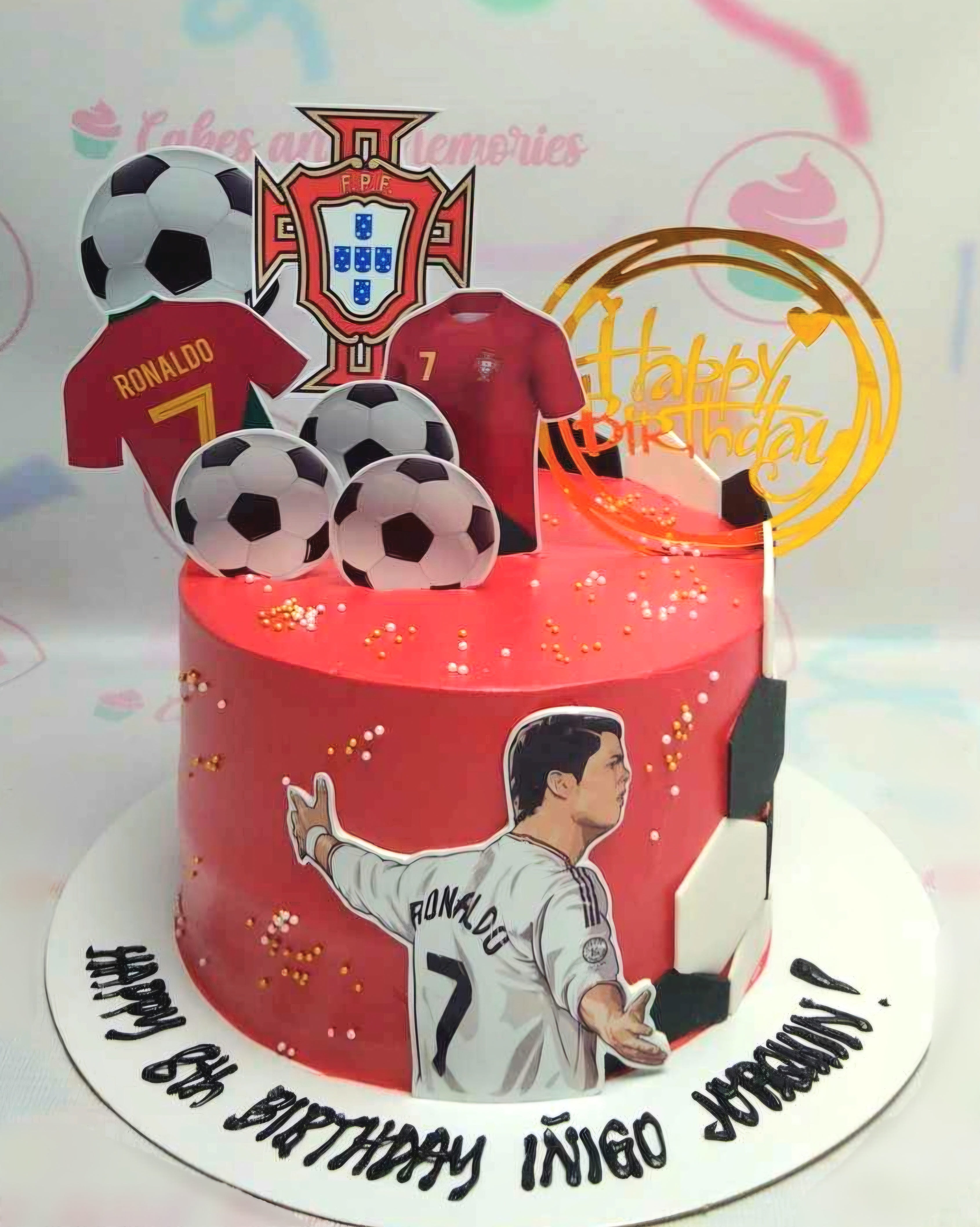 Celebrate a 6th birthday with this custom soccer cake featuring a red soccer football jersey inspired by Cristiano Ronaldo and adorned with soccer balls. The one-tier design showcases printout toppers representing the Portugal National Team, perfect for any young soccer fan.