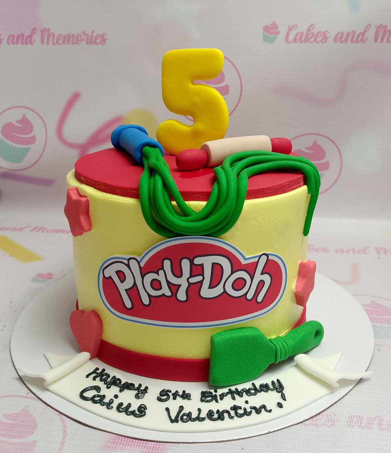 This Playdoh Cake features a colorful design with a number 5 for a 5th birthday celebration, complemented by playful kids' toys and clay molding tools. Topped with themed printout decorations, it's a delightful centerpiece for any young artist's party.