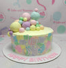 A vibrant 1-tier Rainbow Cake features a pastel yellow base adorned with colorful rainbow-colored balls in blue, red, pink, and green, perfectly capturing a cheerful sky with fluffy clouds. Ideal for birthdays, this customized cake radiates a playful charm with its light colors and a delightful rainbow theme.