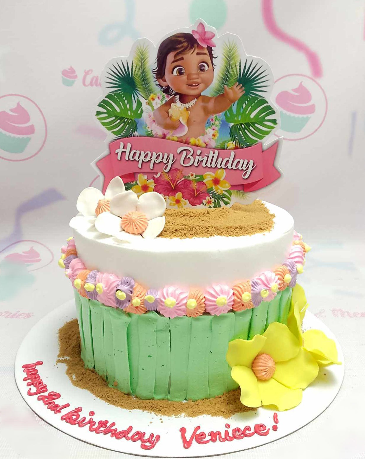 This Moana-themed cake features a stunning design of white, green, and yellow colors with tropical elements like coconut trees and ocean waves. Adorned with printout toppers of Baby Moana and Maui, it captures the essence of a perfect beach celebration for kids' birthdays.