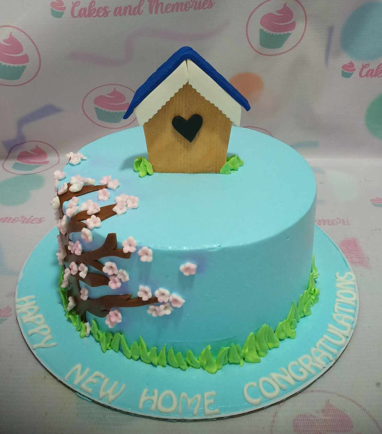 This stunning one-tier house warming cake features a serene blue backdrop adorned with delicate cherry blossom accents, perfect for celebrating the joy of a new home. A customizable design that conveys warm congratulations and blessings for the occasion.