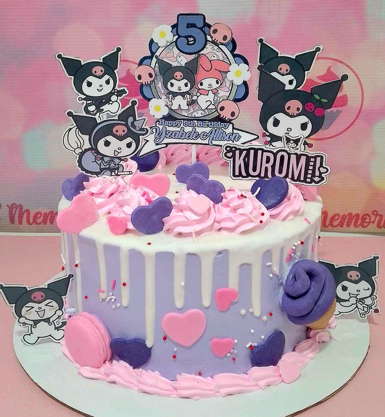 This adorable Kuromi Cake features a delightful blend of purple and pink hues, adorned with hearts and a glossy white drip. Topped with colorful sprinkles, macarons, and playful printout toppers, it perfectly captures the essence of cute Sanrio characters like My Melody and Hello Kitty.