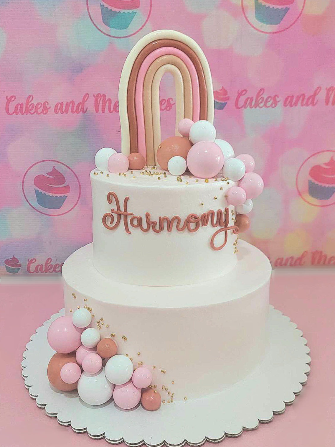 This charming Rainbow (Boho) Cake features a delightful mix of pink, brown, and peach hues, creating a harmonious design. Adorned with a whimsical edible rainbow topper and cute printout toppers, this 2-tier cake is perfect for any birthday celebration, highlighted by elegant shabby chic details and playful white balls.