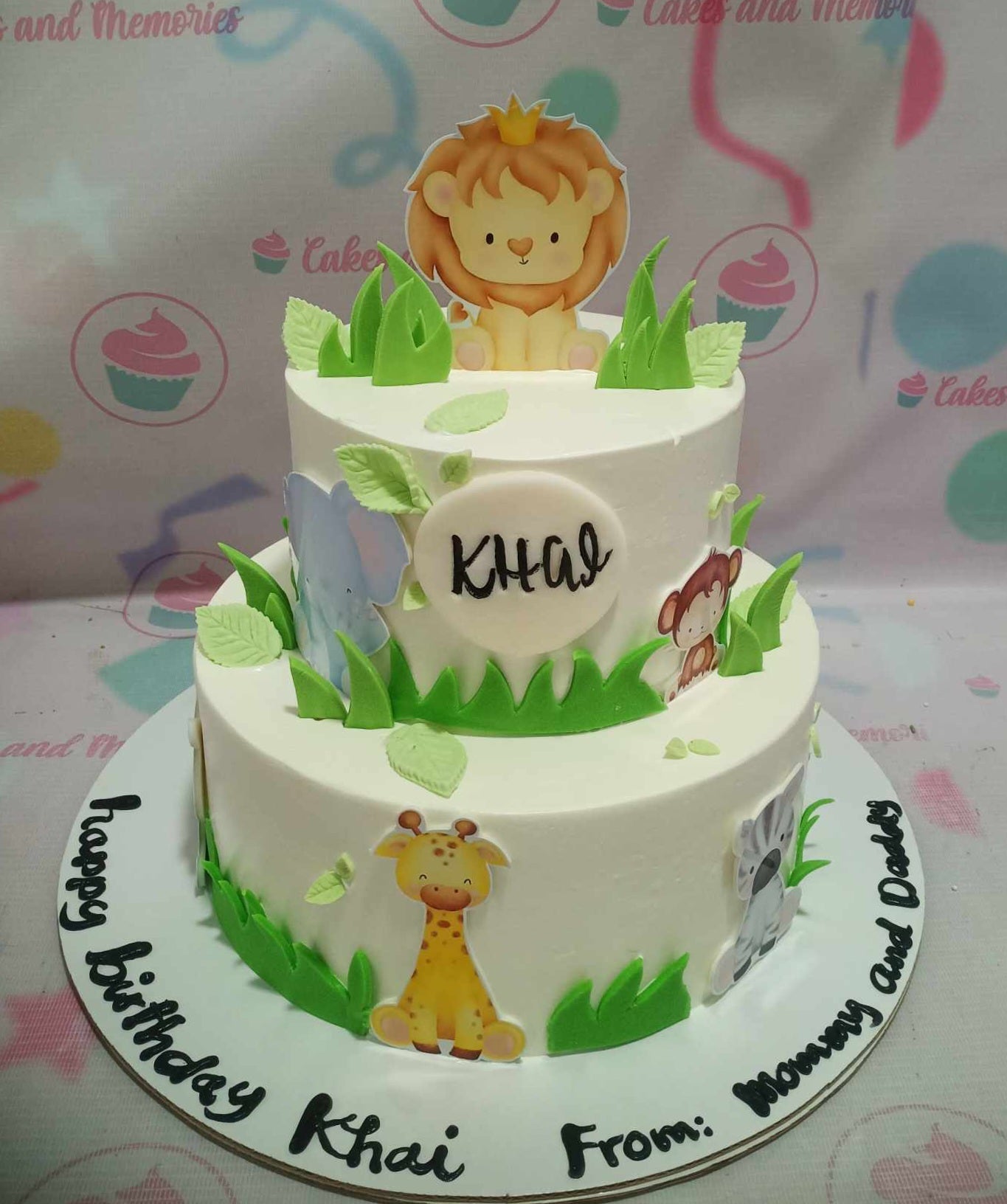 This adorable Safari Cake features two layers adorned with green grass and cute animal printout toppers, including a giraffe, lion, and monkey, perfect for celebrating a "wild one" first birthday. The white and green color palette emphasizes a lively jungle theme, making it a standout centerpiece for any birthday celebration.