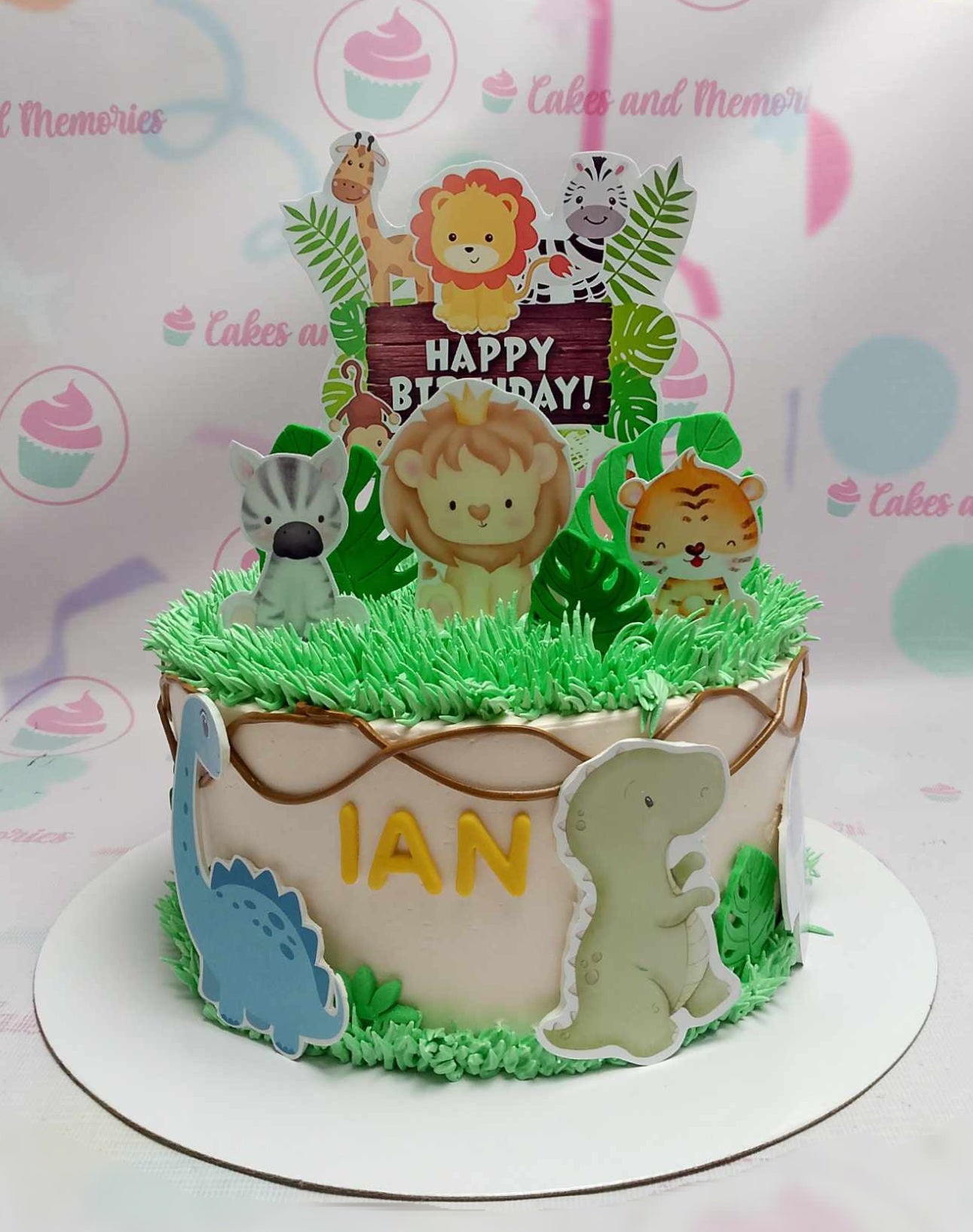 This charming Safari Cake features a playful design with a white base adorned with jungle animals like a lion, zebra, tiger, giraffe, and a cute dinosaur topper. Surrounded by green grass and leaves, it’s perfect for celebrating a baby boy's 1st birthday.