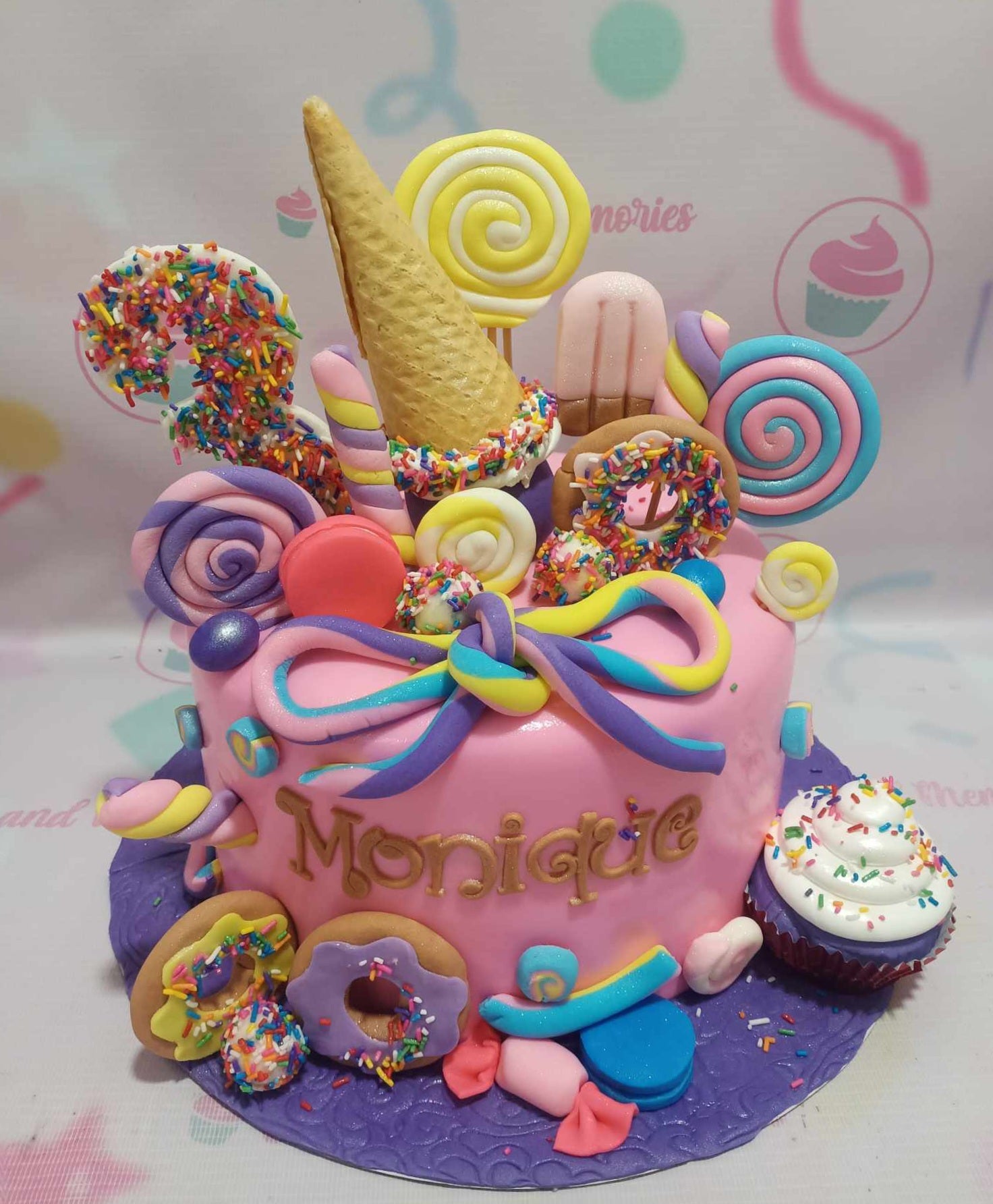 This colorful Candyland Cake features vibrant pink and purple fondant, perfect for a 3rd birthday celebration. Adorned with playful donuts, lollipops, and ice cream, it’s a delightful centerpiece wrapped in a sweet ribbon.