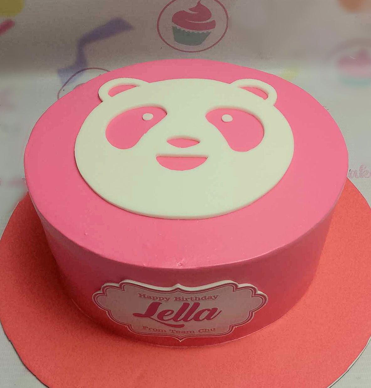 A delightful pink Foodpanda Cake featuring a playful panda design with ears and eyes, perfect for Lella's birthday celebration. Presented on a red plate, this one-tier treat is adorned with themed printout toppers from Team Chu.