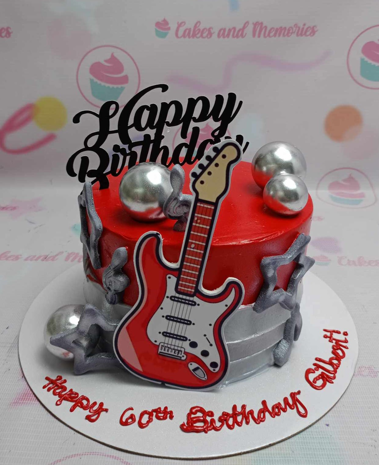 This custom Music Cake features a striking red electric guitar centerpiece, adorned with silver balls and star accents, perfect for celebrating Gilbert's 60th birthday. The one-tier design includes rock and roll-themed printout toppers, making it a memorable tribute for dad, grandad, or papa's special day.