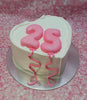 This beautiful heart-shaped Love Cake features smooth white icing adorned with pink ribbons and a cheerful pink balloon. Perfect for a 25th birthday celebration, it proudly displays the number 
