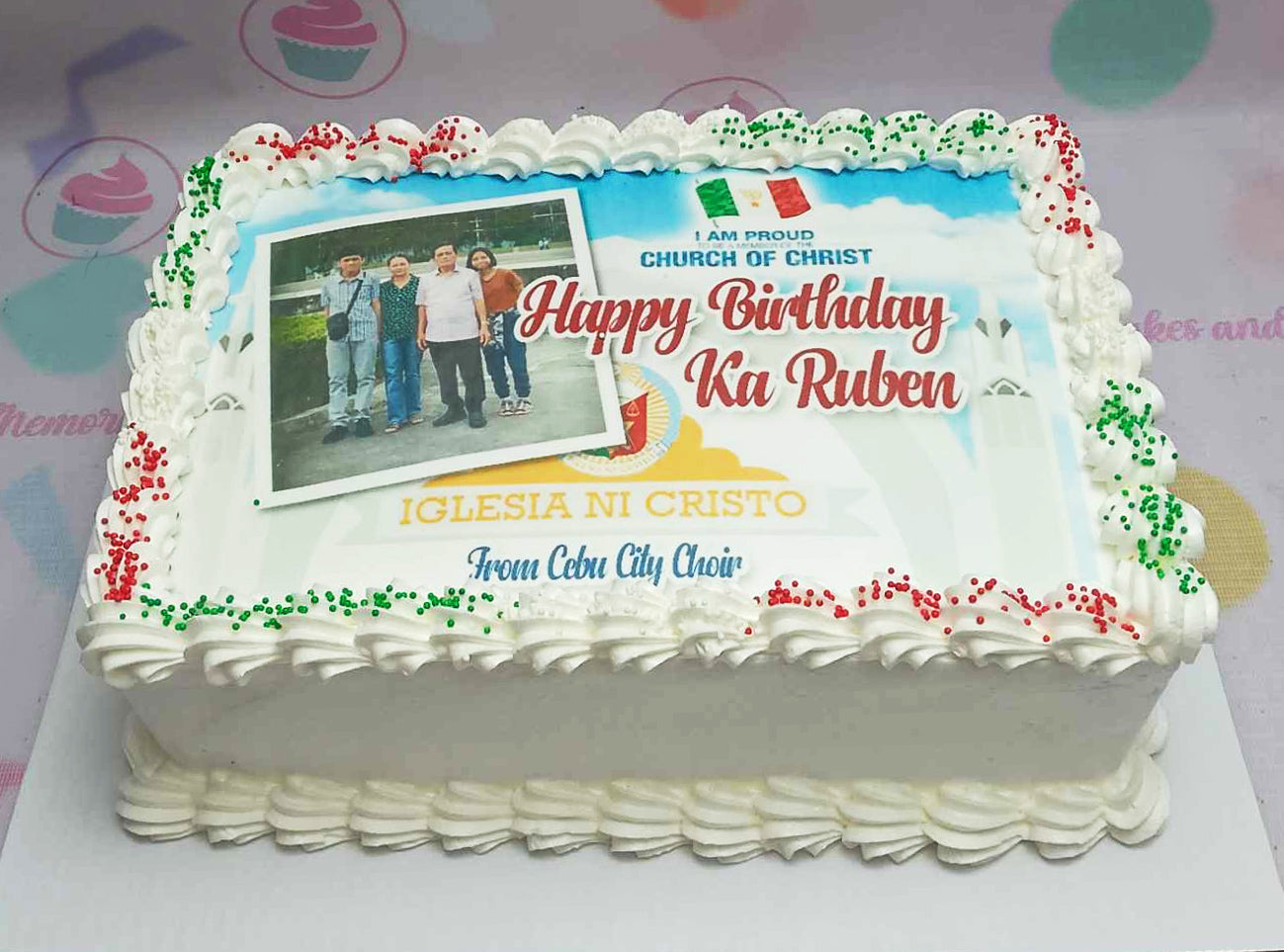 This rectangular Edible Photo Birthday Cake features a striking design with white, blue, green, and red colors, adorned with colorful sprinkles. The edible photo prominently showcases the Iglesia Ni Cristo choir, perfect for a special celebration in Cebu City.