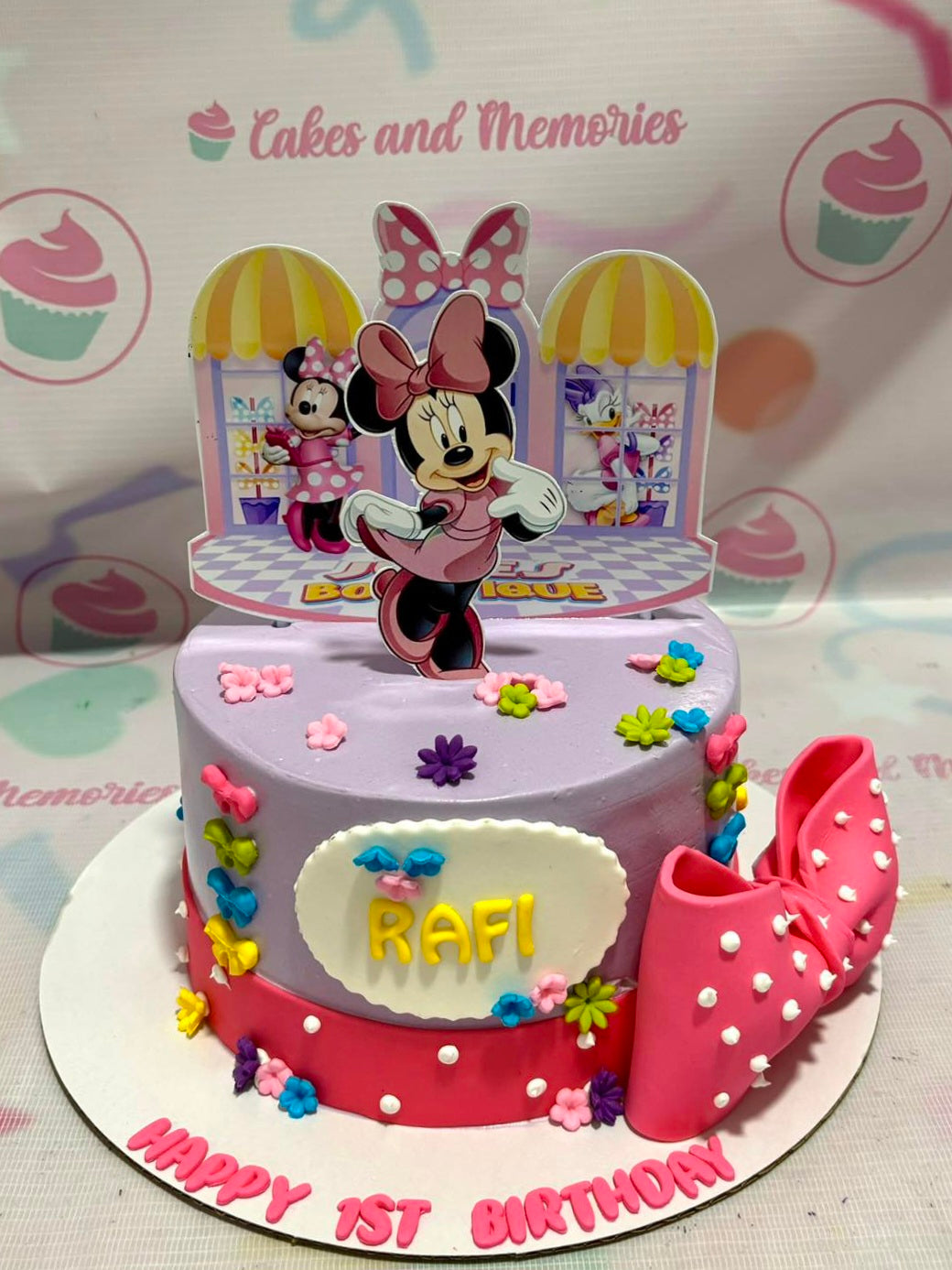 A delightful Minnie Mouse cake featuring a vibrant purple and pink color scheme, adorned with a pink edible topper ribbon and printout Minnie Mouse toppers. This charming one-tiered cake is perfect for children's birthday celebrations.