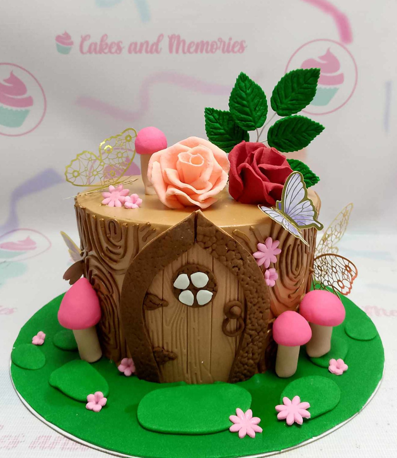 This charming fairy cake features a brown tree door surrounded by delicate mushrooms, colorful flowers, and green leaves, complete with a butterfly and a fairy girl design perfect for a first birthday. The cake, styled with gold and pink accents on a wood-like base, showcases a delightful 1-tier, 1-layer creation adorned with printout toppers.