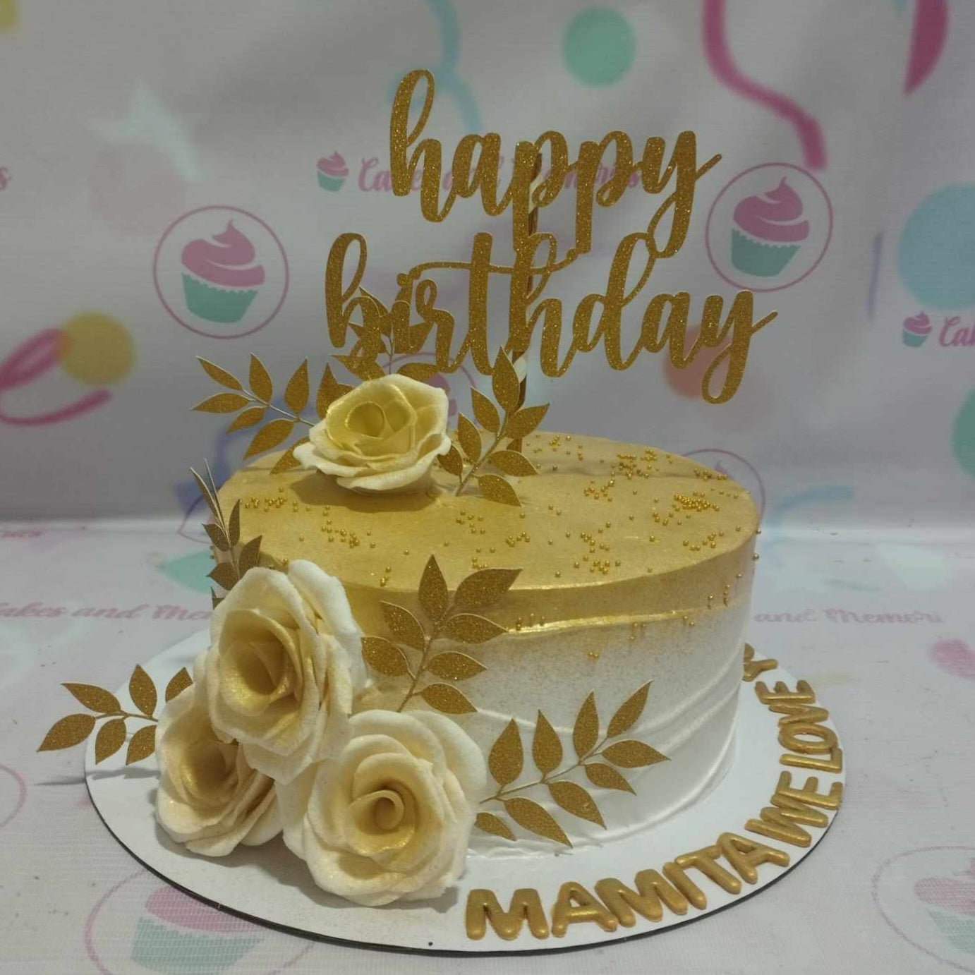 A stunning white floral cake decorated with delicate white flowers and elegant golden leaves, topped with a shining gold "Happy Birthday" topper. This one-tier cake is perfect for celebrating an 18th birthday, featuring printout toppers and a sophisticated design.