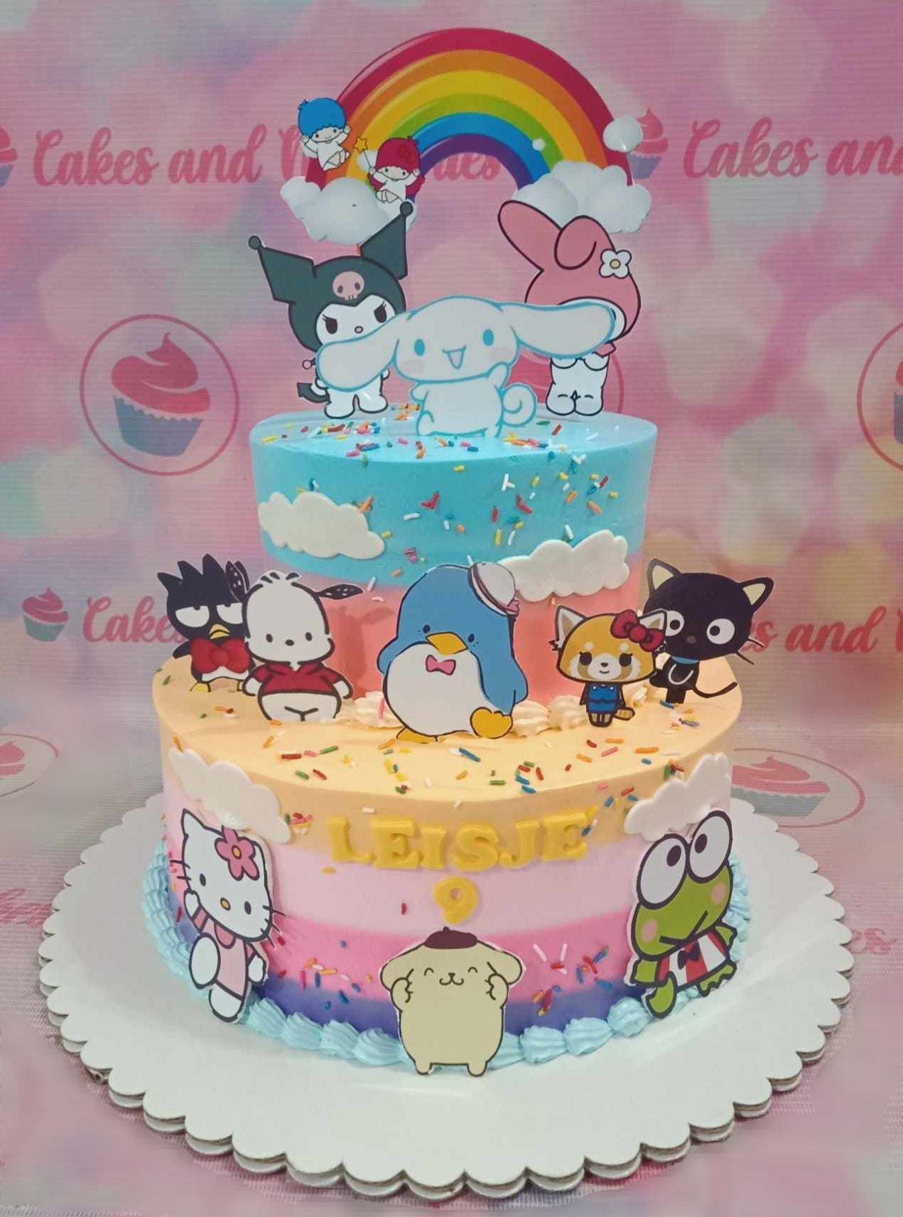 This vibrant Hello Kitty cake features whimsical multi-tiers adorned with frosted icing in colorful pastel shades of pink, blue, and yellow. Topped with cute cartoon printouts of Sanrio characters like Keroppi, Pochacco, and Kuromi, it's the perfect centerpiece for any birthday celebration.