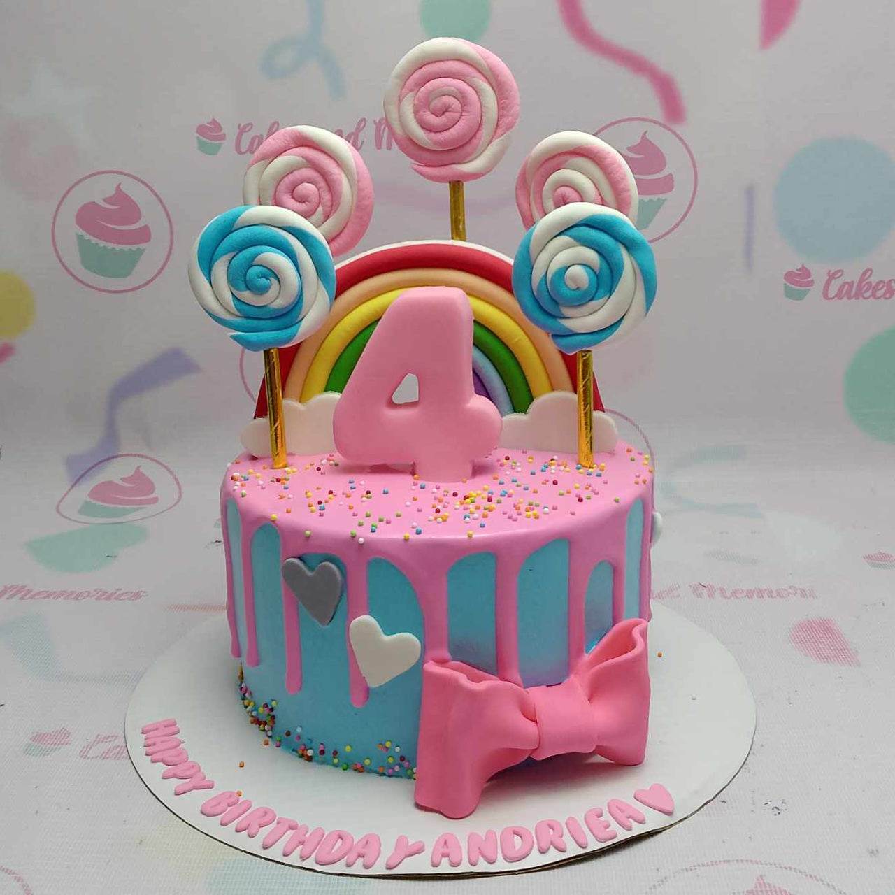 Celebrate a special 4th birthday with this vibrant 1-tier drip cake featuring a delightful pink drip, accented by a blue hue and adorned with colorful lollipop and rainbow toppers. Finished with a charming pink ribbon, this customized creation is perfect for any festive occasion.