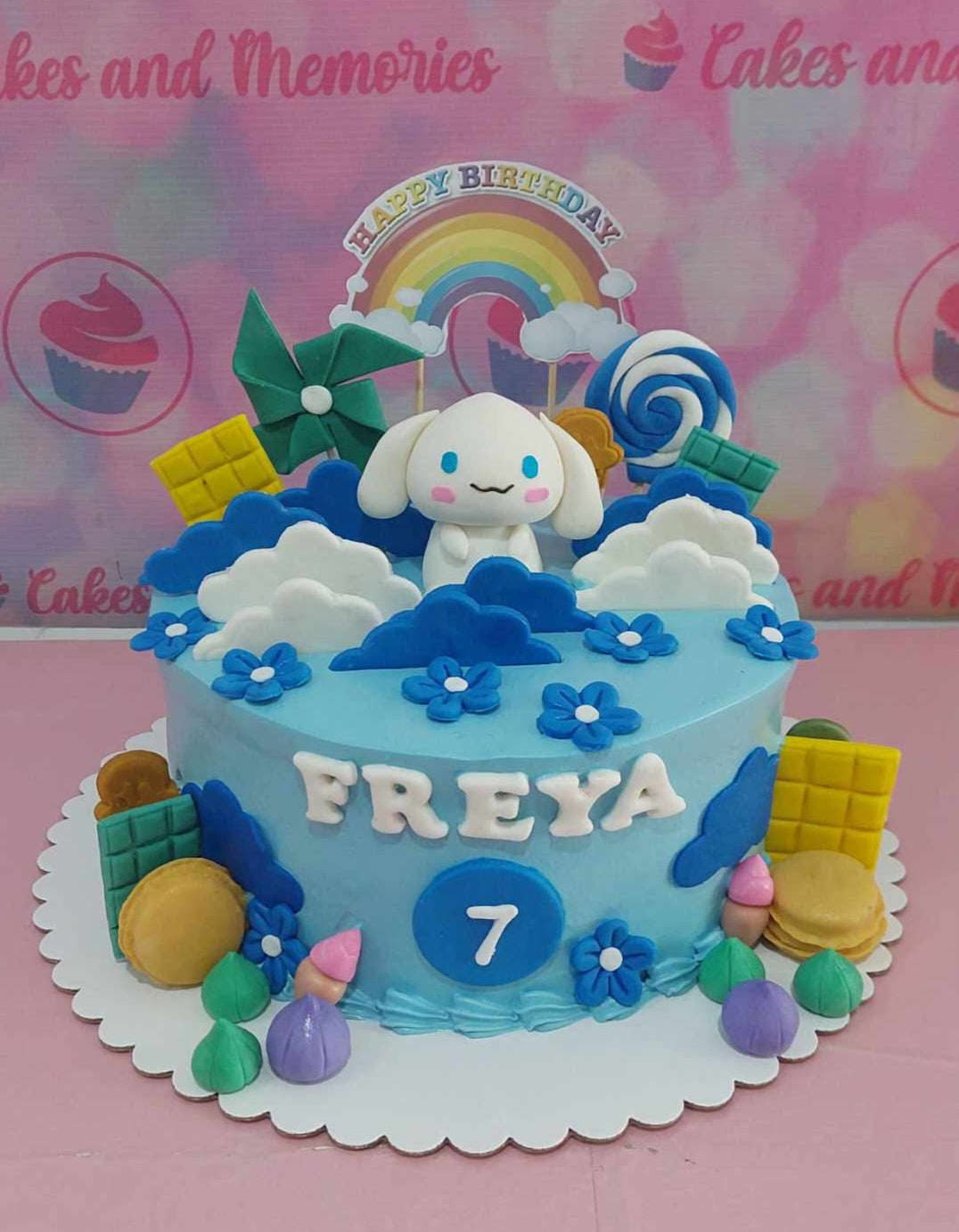 This adorable Cinnamoroll Cake features a playful design with a bright blue base, colorful rainbow printouts, fluffy clouds, and whimsical pinwheels. Perfect for any Sanrio fan, this one-tier cake is adorned with lollipops and captures the essence of Candyland.