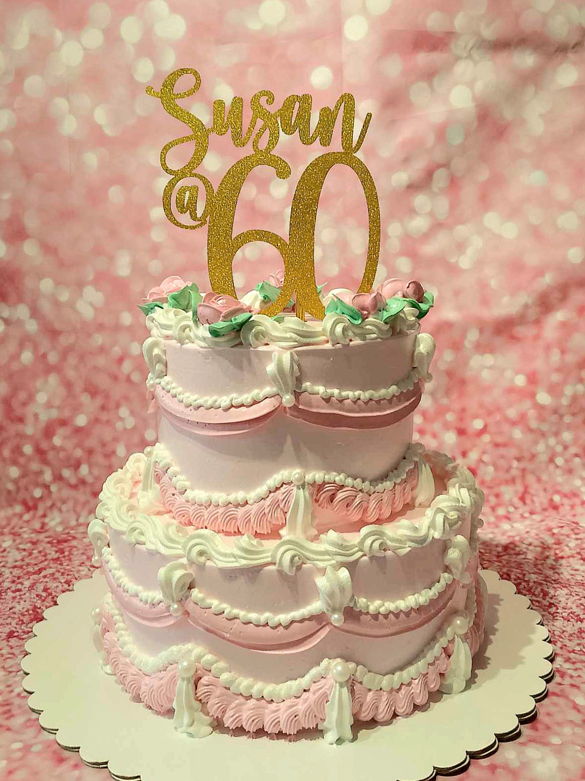 A stunning two-tiered vintage cake in soft pink, elegantly adorned with delicate flowers and pearls. Perfect for celebrating a 60th birthday, honoring a beloved mama or grandmother.