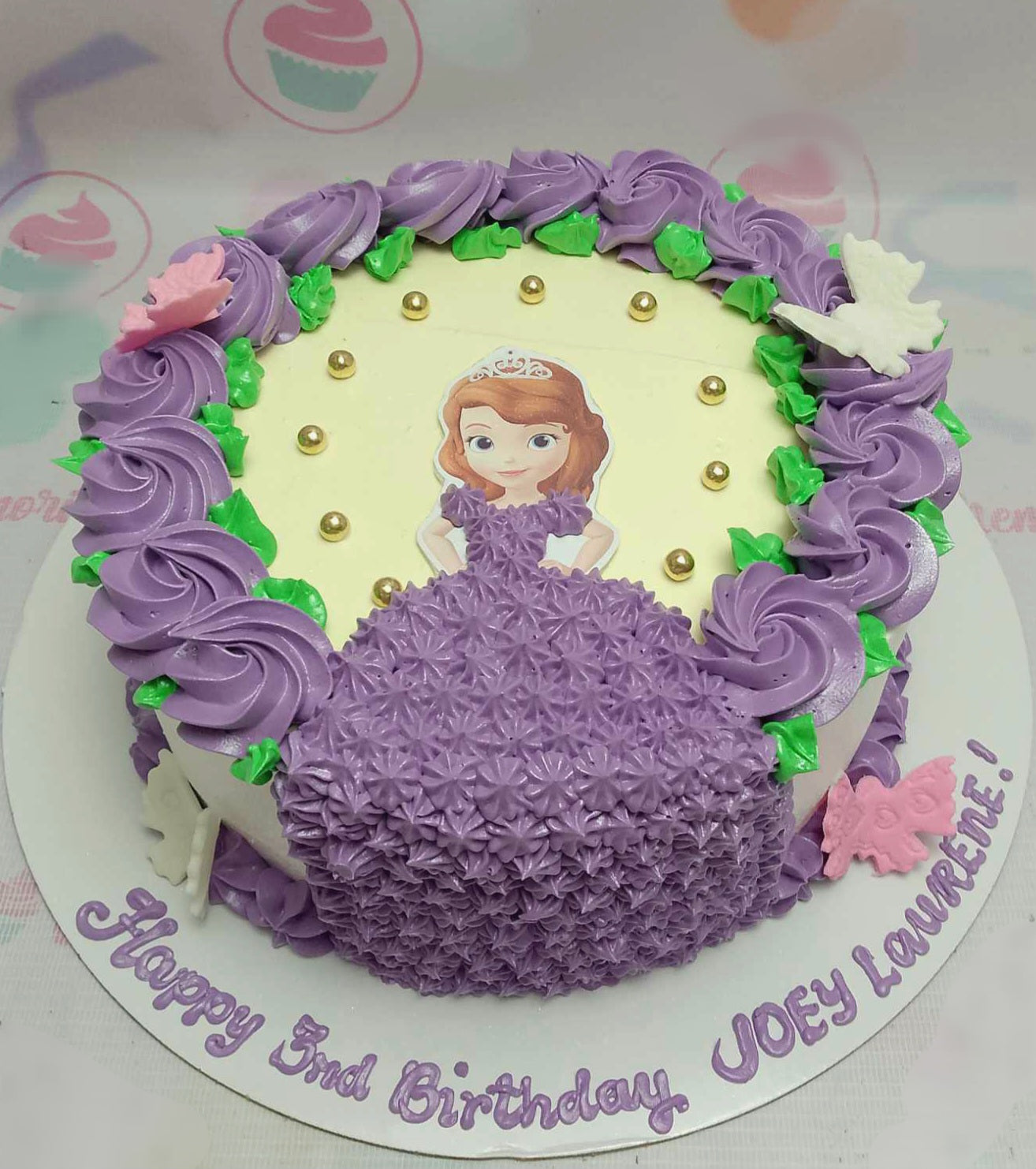 Celebrate a magical 3rd birthday with this stunning Sofia Cake, featuring vibrant purple rosette icing and whimsical floral decorations. Adorned with butterfly printout toppers, this one-tier princess cake is perfect for any Sofia the First fan.