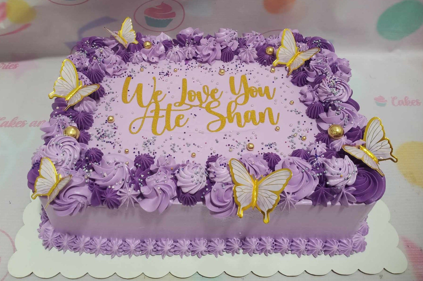 A stunning rectangular Butterflies Cake adorned with vibrant purple and violet hues features delicate butterfly decorations and a shimmering gold topper. Perfect for birthday celebrations, this customized sheet cake is a beautiful centerpiece for any occasion.