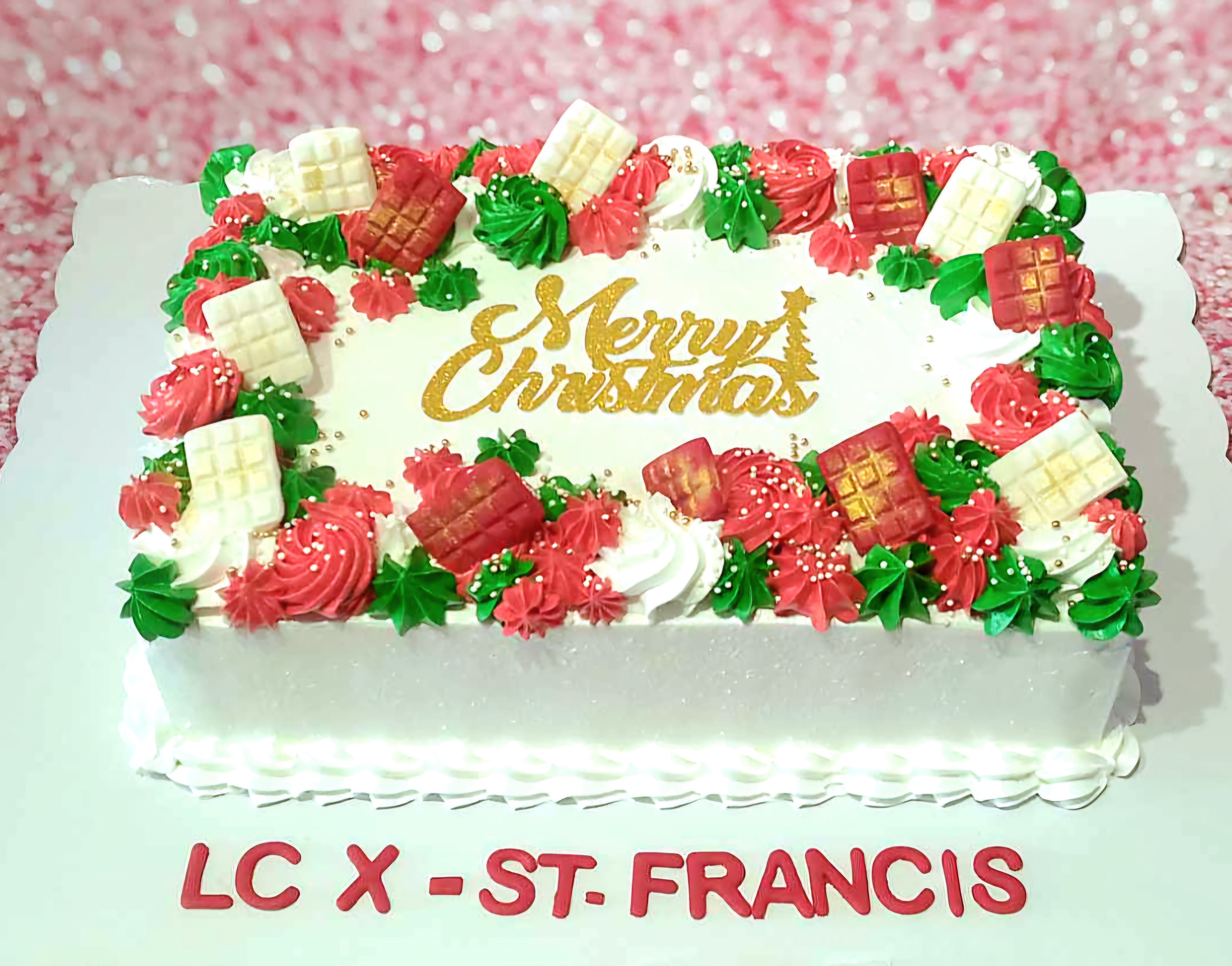 This festive rectangular Christmas cake features a smooth white frosting adorned with red and green swirls, complemented by chocolate pieces. Perfect for any holiday party, it sends warm wishes with "Merry Christmas" elegantly written on top.