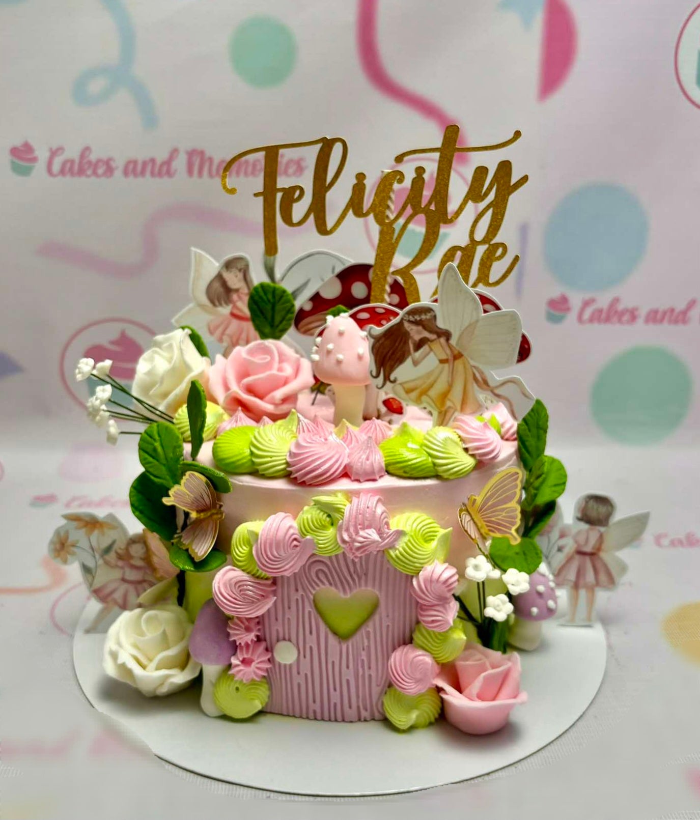 This enchanting 1-tier fairy cake features a pink color palette adorned with butterflies, mushrooms, and delicate flowers. Topped with gold glitter accents and playful printout toppers, it’s a perfect centerpiece for a girl's 1st birthday celebration.