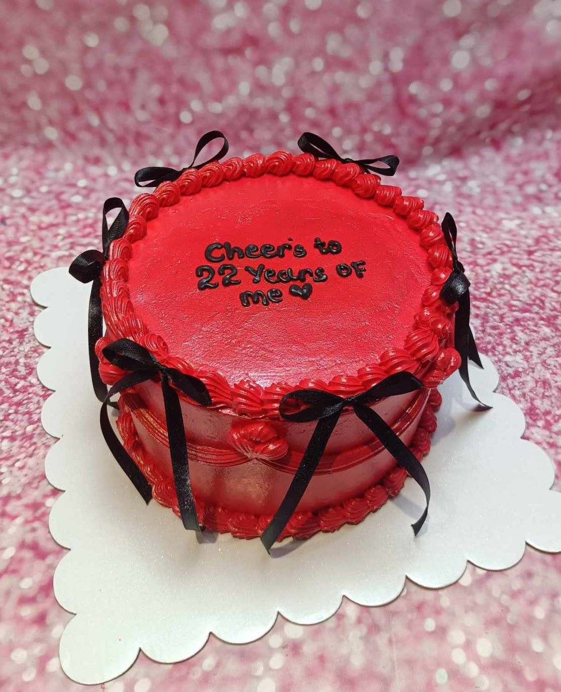 A stunning crimson red ribbon cake with black bows elegantly decorates the top, celebrating "Cheers to 22 years of me." This vintage design features a 1-tier, 1-layer structure, perfect for marking a memorable 22nd birthday.