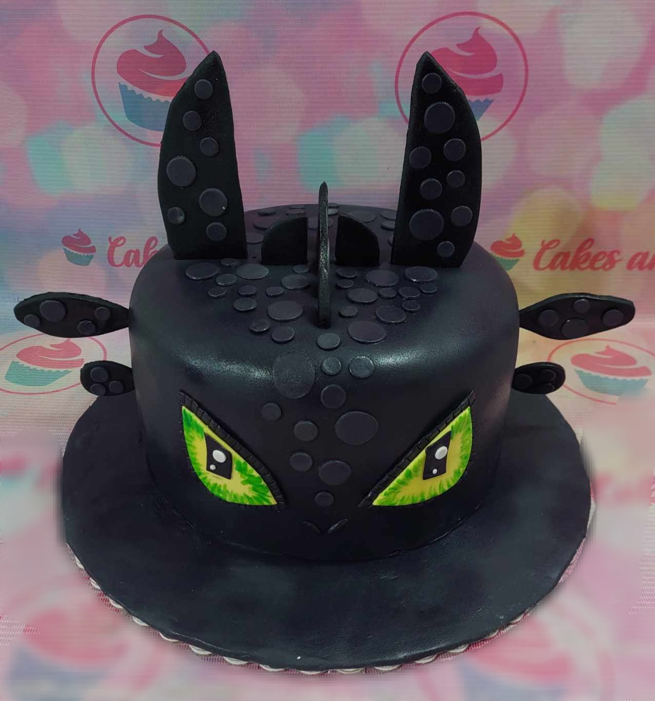 This custom decorated Cartoon Cake features a striking black background adorned with Toothless from "How to Train Your Dragon." Designed as a single-tiered, fondant-covered masterpiece, it showcases printout toppers inspired by animated movies and reptiles.