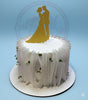 One-tier wedding cake with a gold glitter bride and groom topper, white ruffled sides, and delicate white flowers.