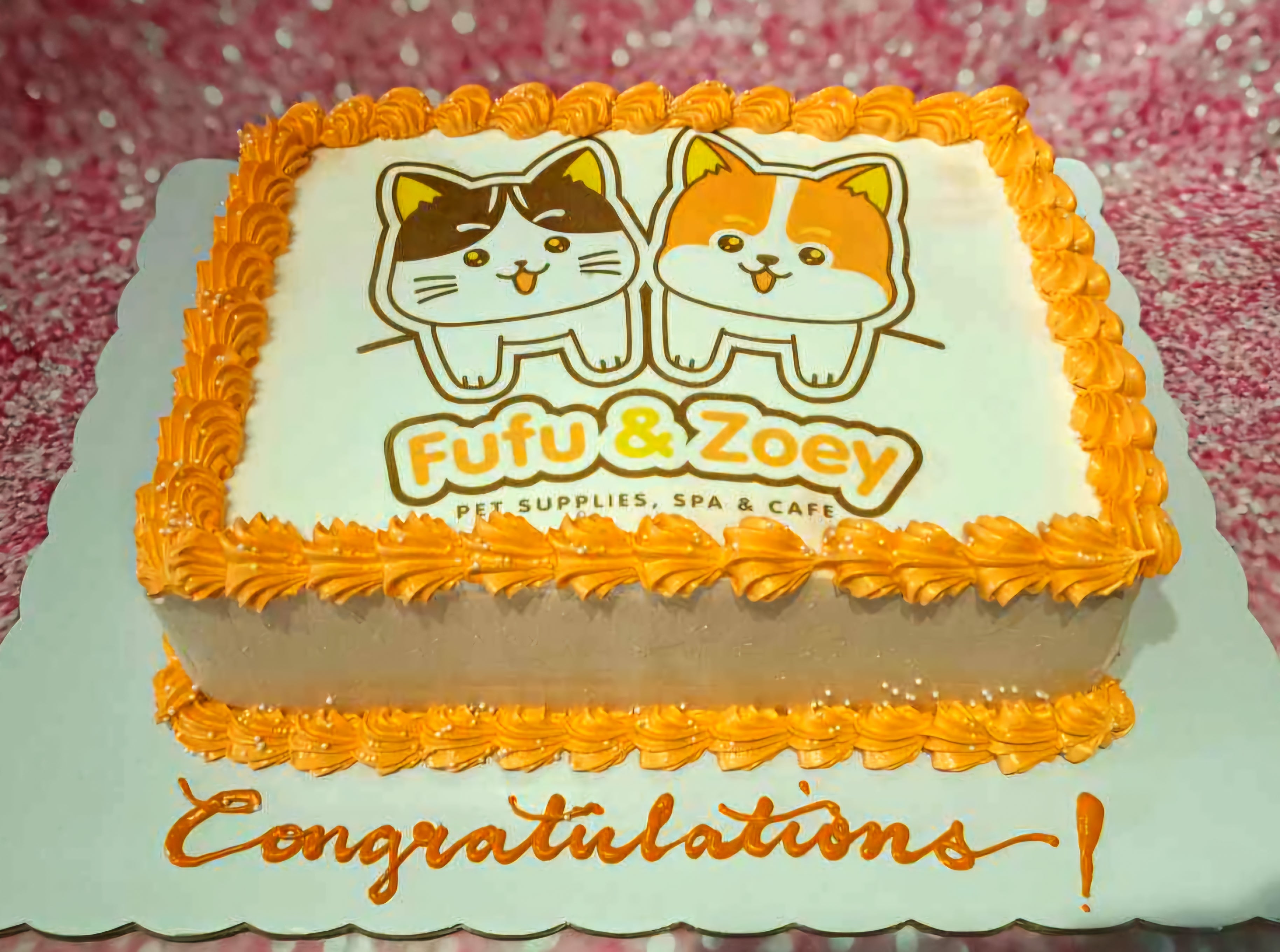 A delightful Congratulations Cake featuring orange and white icing, adorned with a cartoon cute cat and dog named Fufu & Zoey. This rectangular edible photo cake showcases a fun congratulations message tailored for a pet shop.