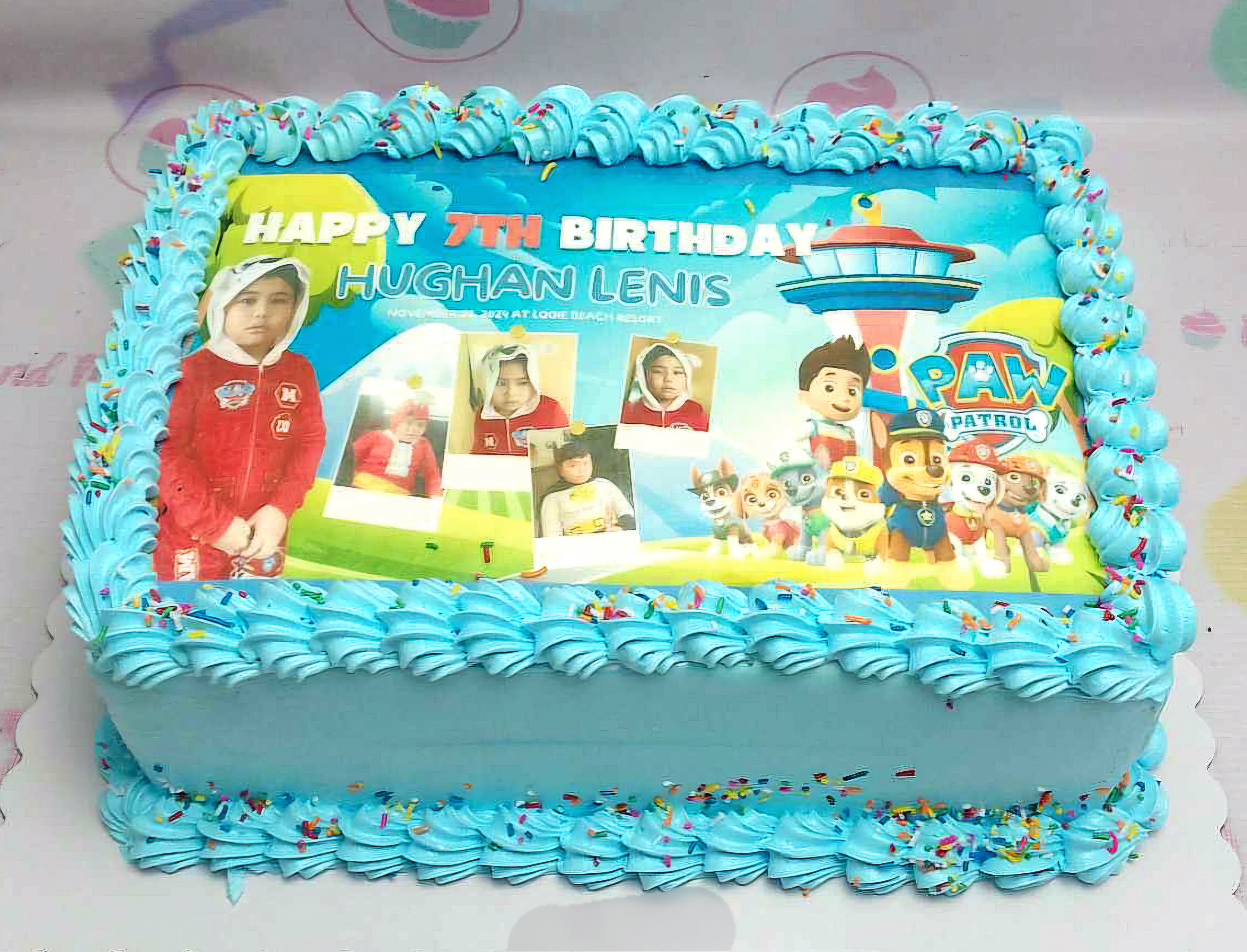 The Paw Patrol cake features a blue rectangular design adorned with colorful candy sprinkles and an edible photo of the beloved characters, perfect for a 7th birthday boy. This custom cake captures the excitement of the occasion with its fun decorations.