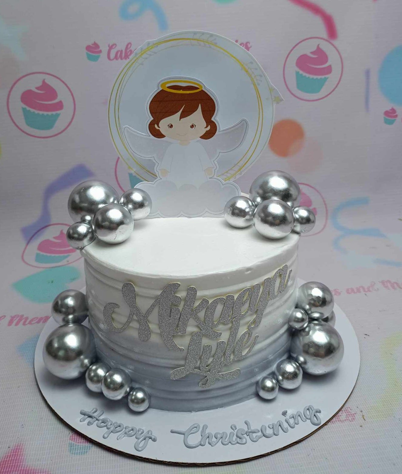 This stunning Christening Angel Cake features a pristine white base adorned with silver balls and a personalized silver glitter name. Topped with a charming angel printout topper, this one-tier, one-layer cake beautifully celebrates a baby girl's baptism or special occasion.